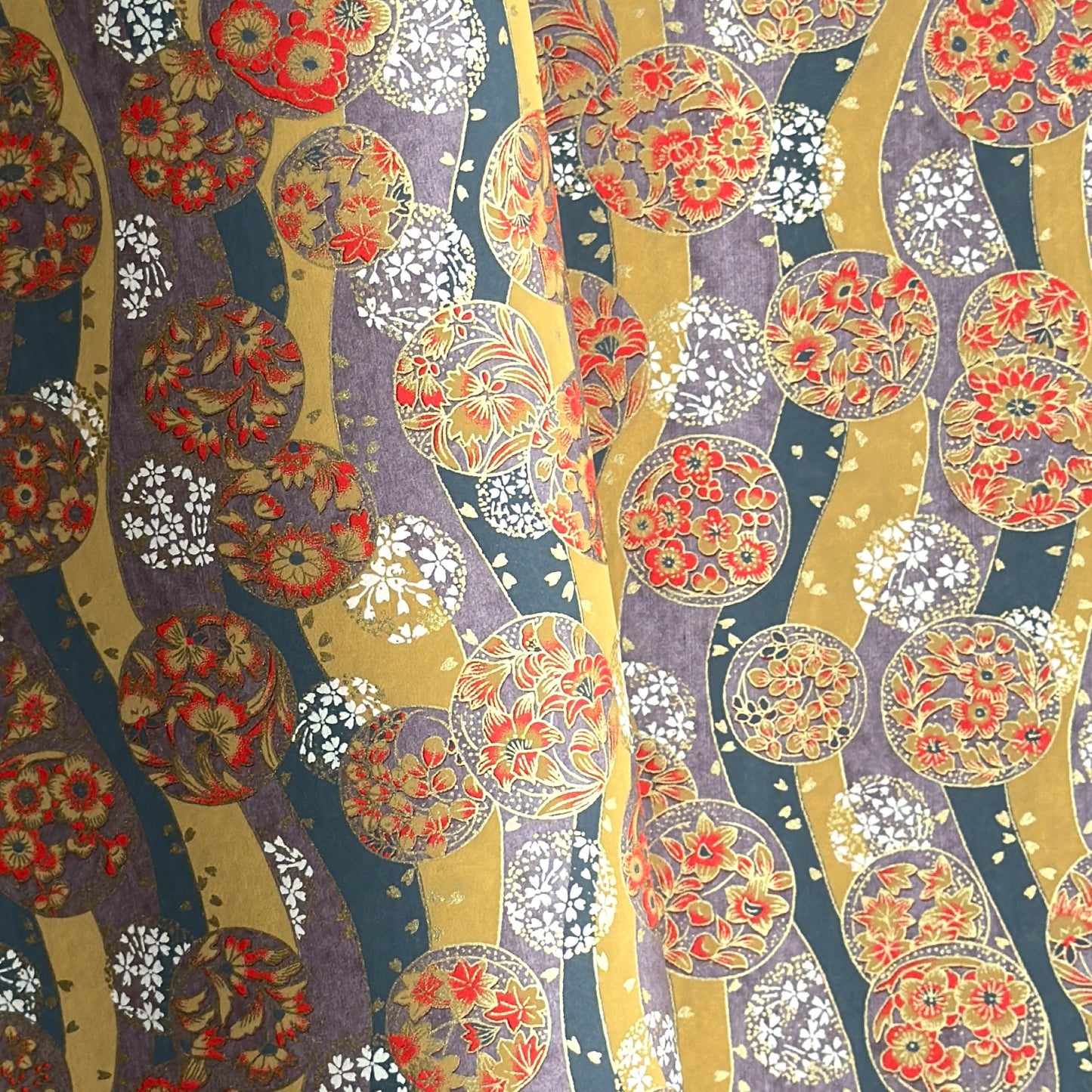 Japanese silkscreen chiyogami paper with a traditional botanical circle motif in tones of mustard, inky blue, lilac and gold.
