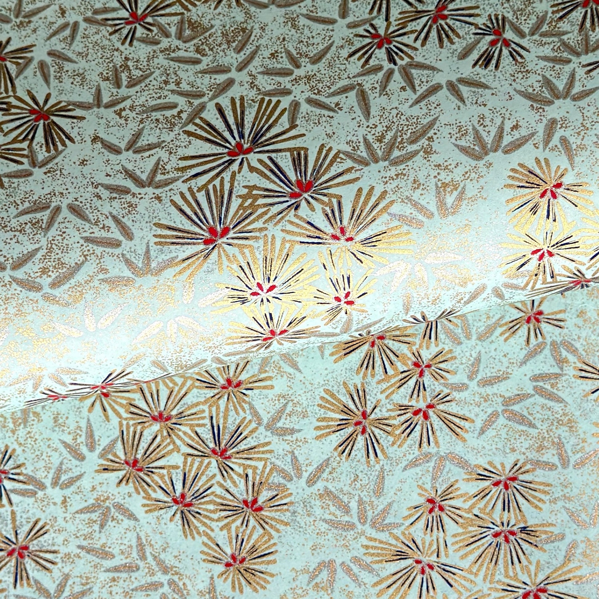 Japanese chiyogami paper silkscreen printed with gold pine needle design on a soft aqua backdrop.