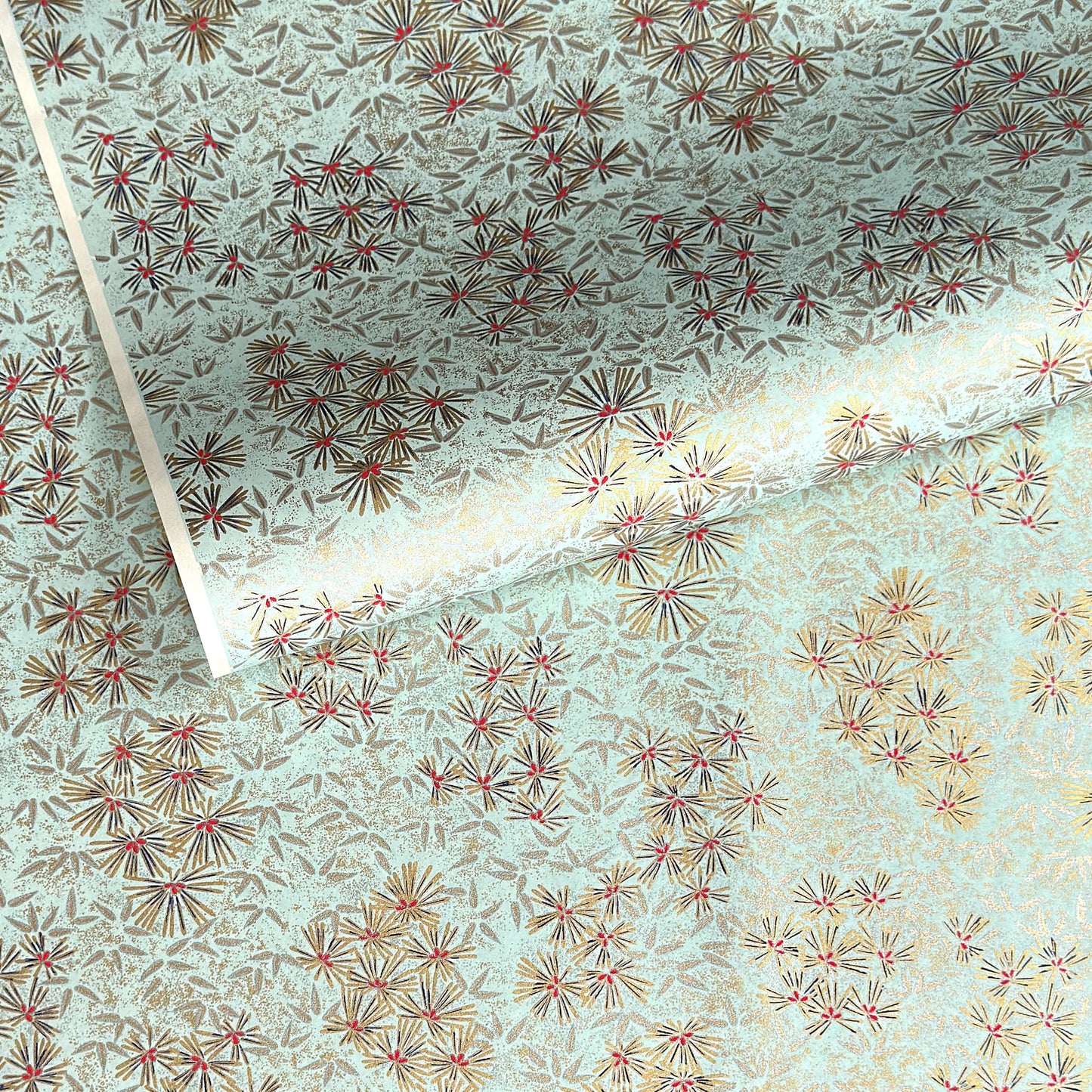Japanese chiyogami paper silkscreen printed with gold pine needle design on a soft aqua backdrop.