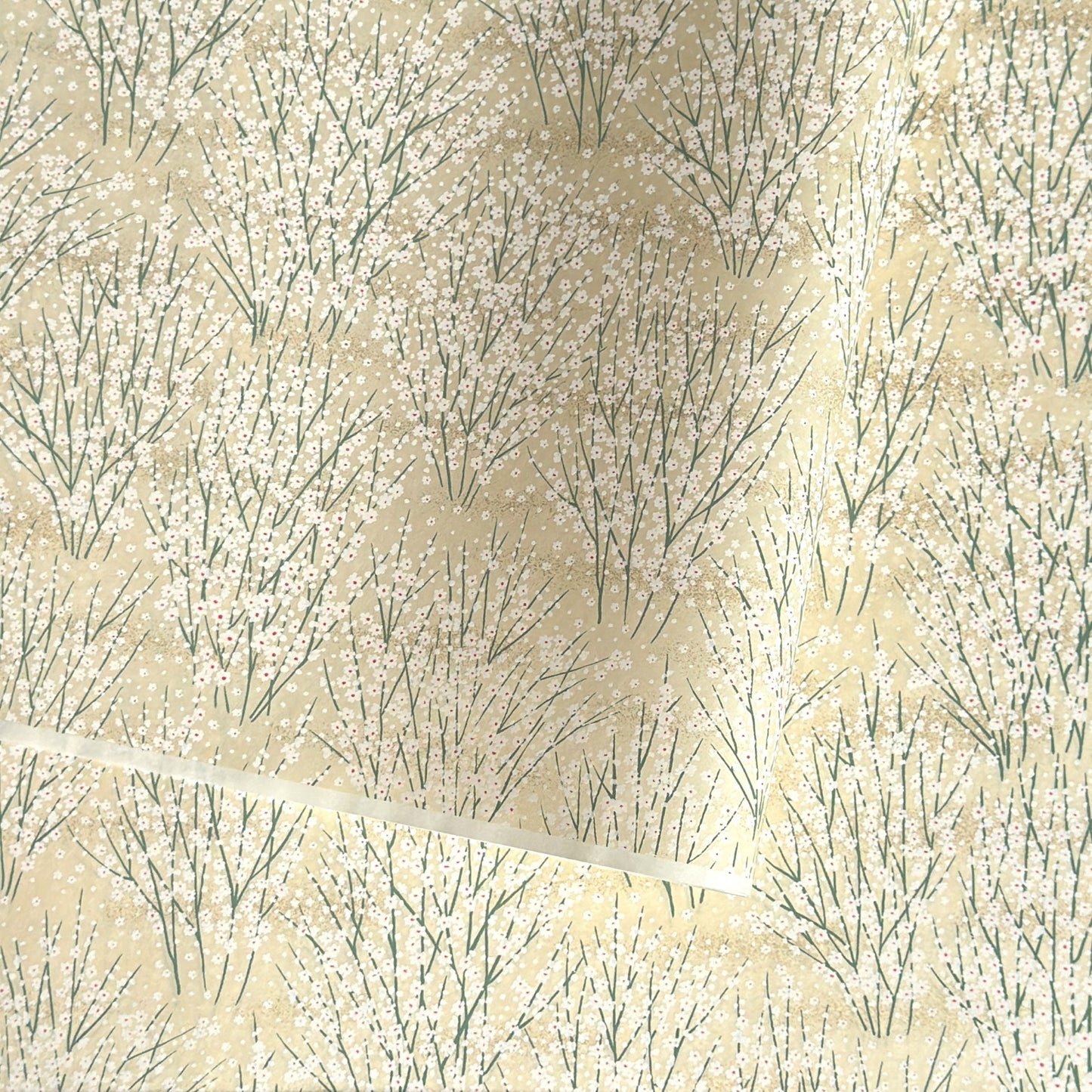 a sheet of Japanese silkscreen printed chiyogami paper with a delicate design of tufts of meadow grasses in flower in white, green on a cream background
