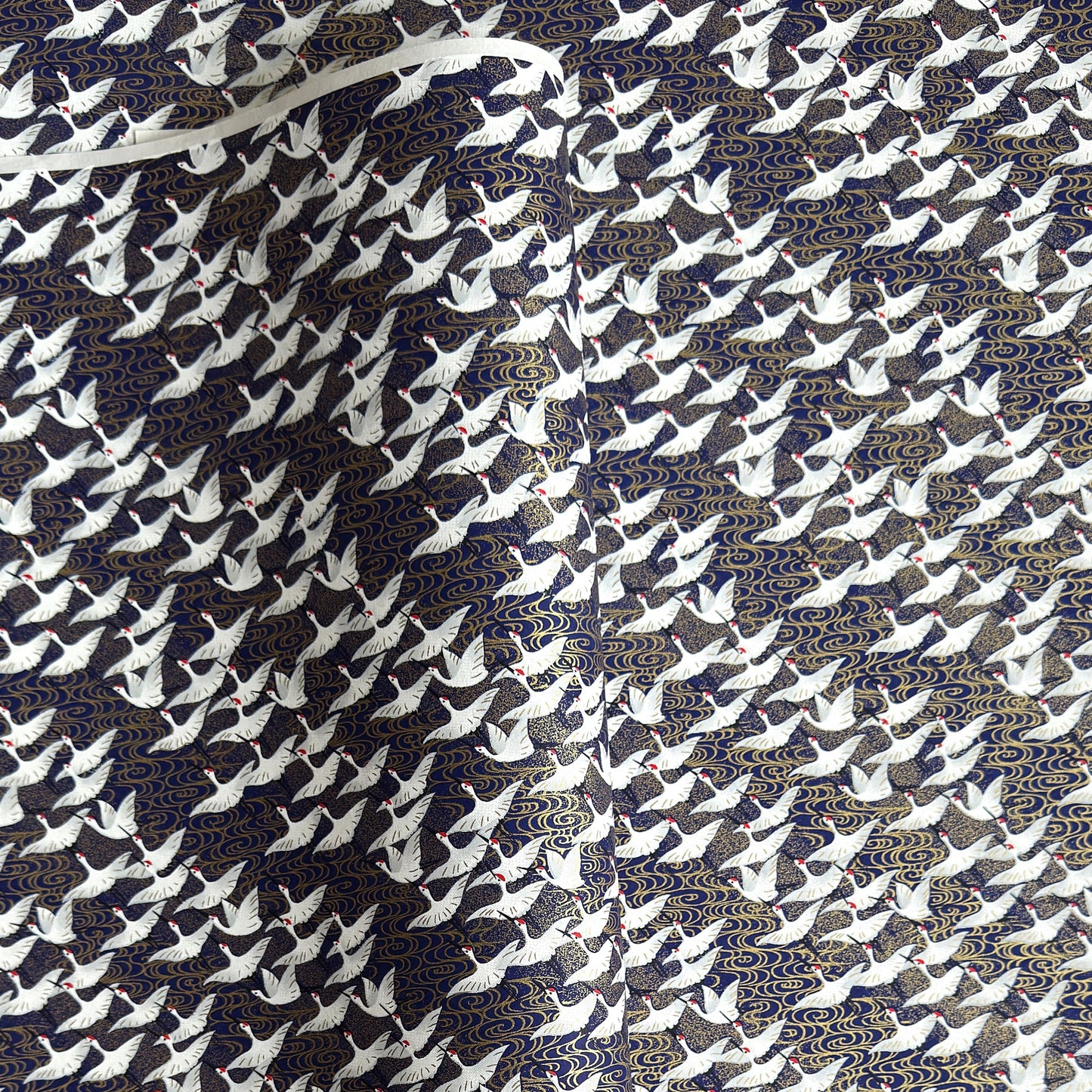 Japanese chiyogami paper with a silkscreened pattern of white cranes in flight on a midnight blue and gold background.