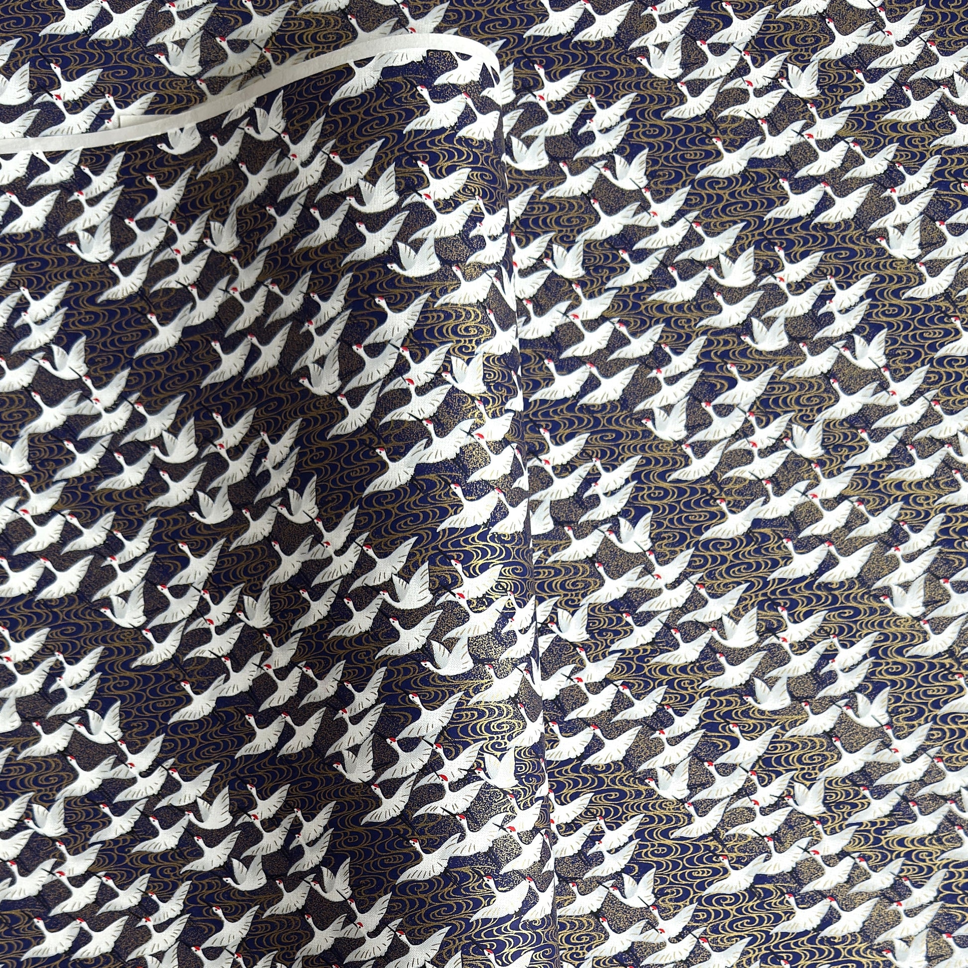 Japanese chiyogami paper with a silkscreened pattern of white cranes in flight on a midnight blue and gold background.