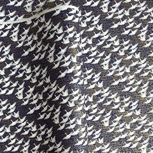 Japanese chiyogami paper with a silkscreened pattern of white cranes in flight on a midnight blue and gold background.