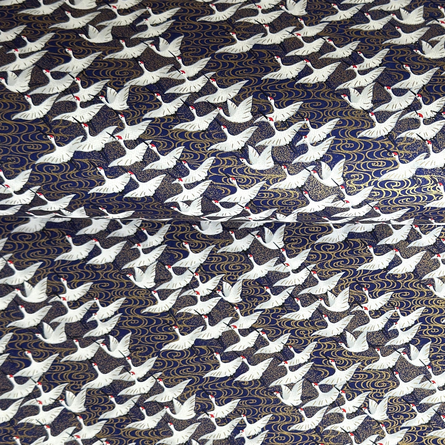 Japanese chiyogami paper with a silkscreened pattern of white cranes in flight on a midnight blue and gold background.