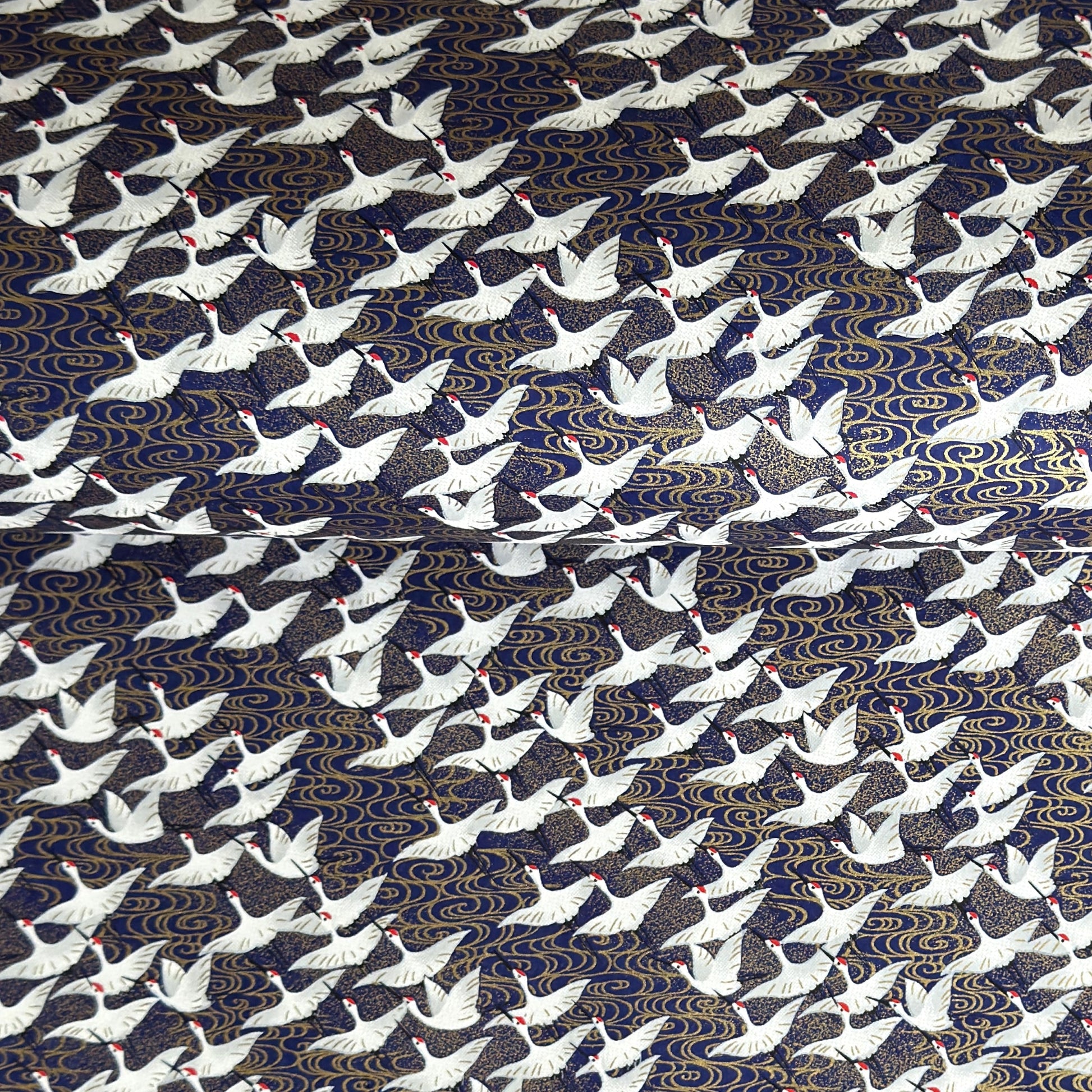 Japanese chiyogami paper with a silkscreened pattern of white cranes in flight on a midnight blue and gold background.