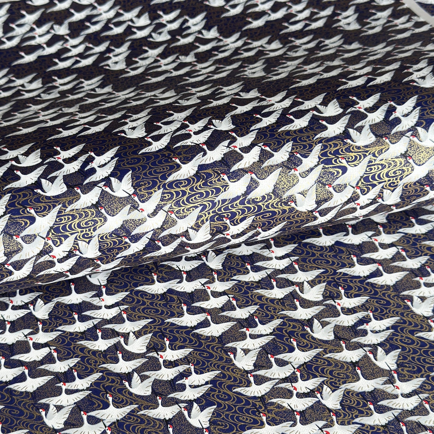 Japanese chiyogami paper with a silkscreened pattern of white cranes in flight on a midnight blue and gold background.