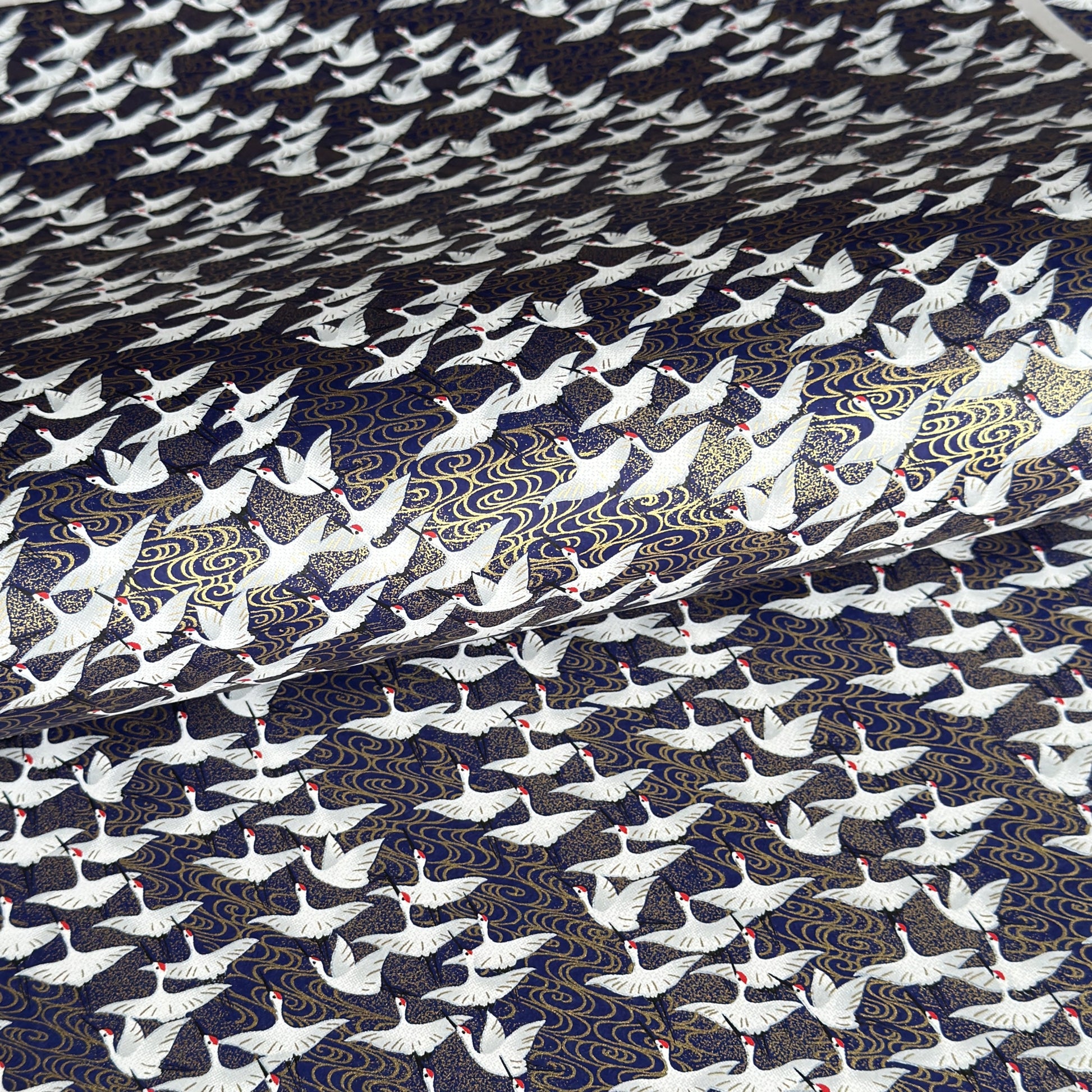 Japanese chiyogami paper with a silkscreened pattern of white cranes in flight on a midnight blue and gold background.