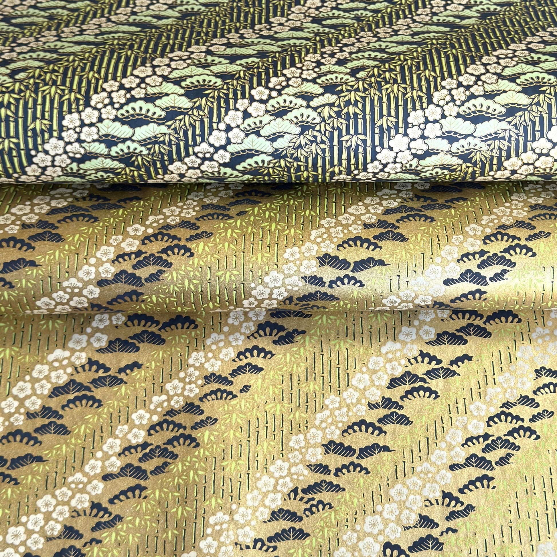 Japanese chiyogami paper with a design of trees, bamboo and plum blossom in indigo, green and white on a vintage gold backdrop. 