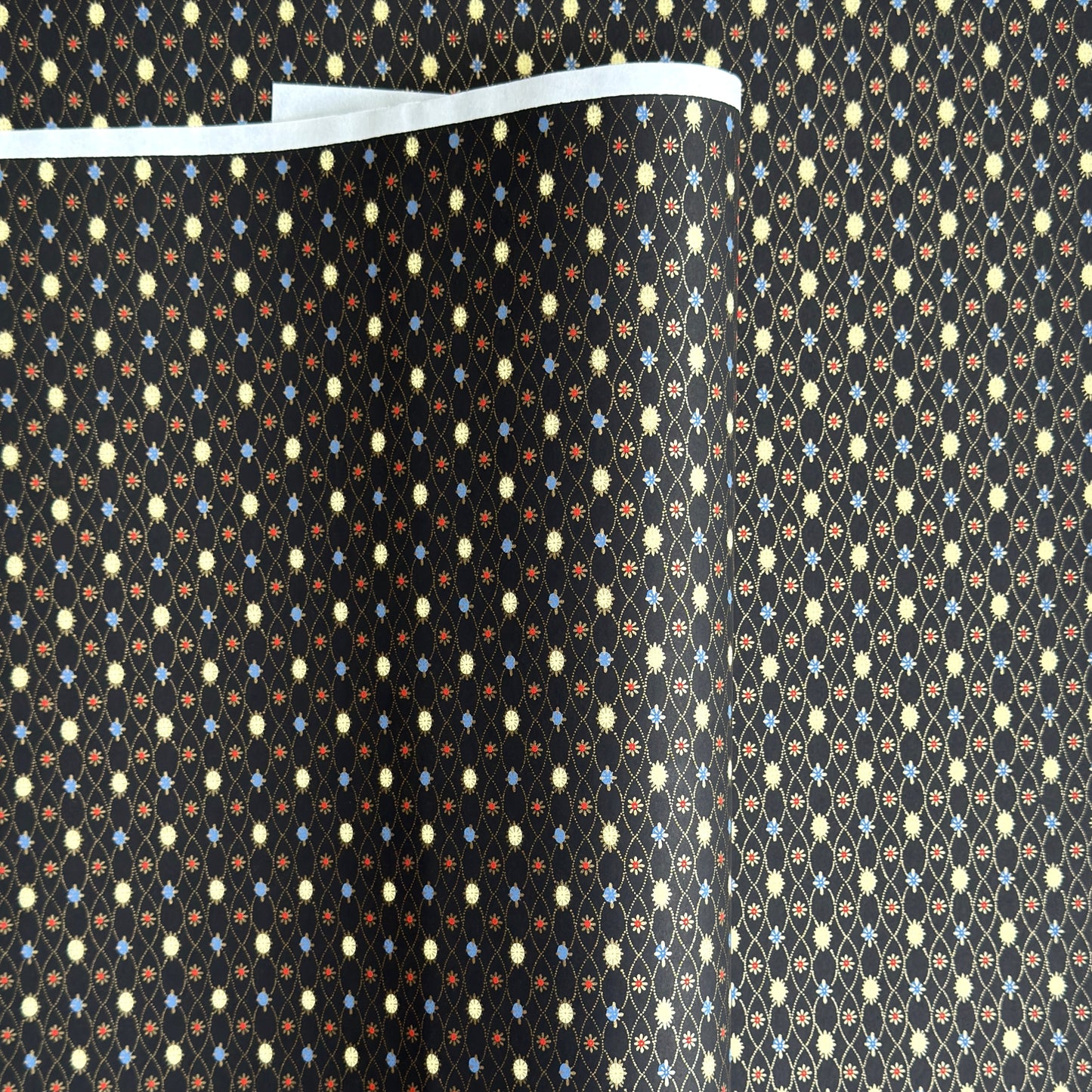Japanese silkscreen chiyogami paper with a pattern of small repeat motifs in red, blue, lemon and gold on a black background