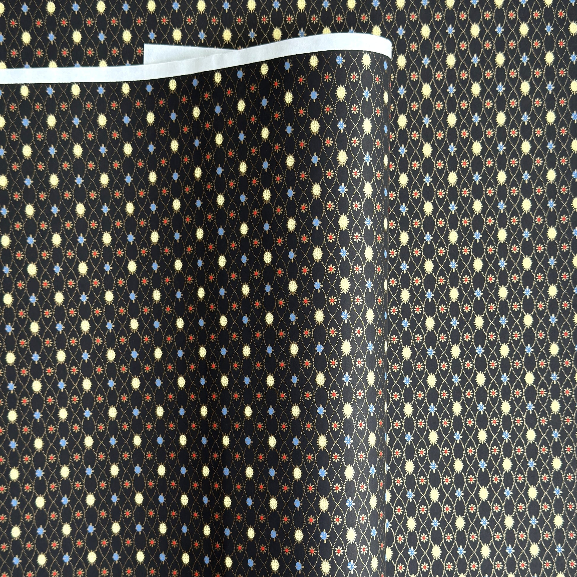 Japanese silkscreen chiyogami paper with a pattern of small repeat motifs in red, blue, lemon and gold on a black background