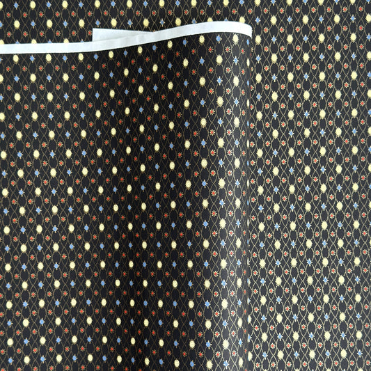 Japanese silkscreen chiyogami paper with a pattern of small repeat motifs in red, blue, lemon and gold on a black background