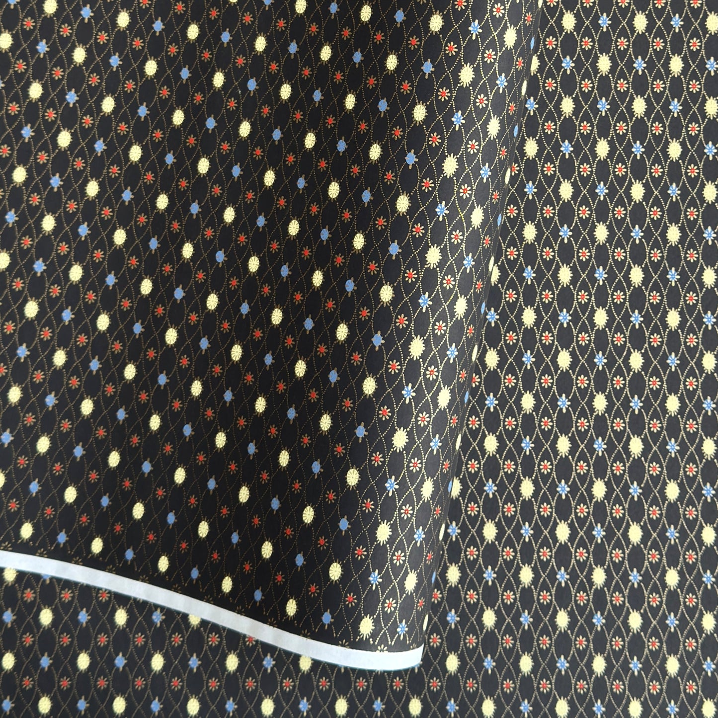 Japanese silkscreen chiyogami paper with a pattern of small repeat motifs in red, blue, lemon and gold on a black background