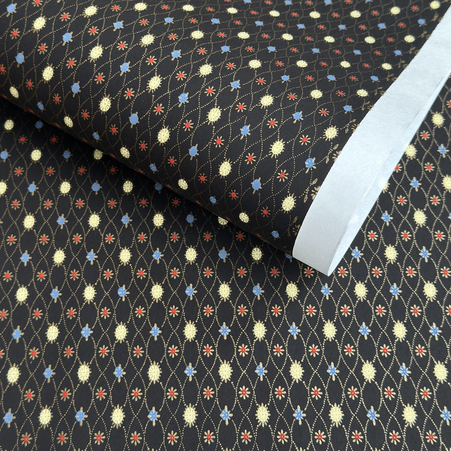 Japanese silkscreen chiyogami paper with a pattern of small repeat motifs in red, blue, lemon and gold on a black background