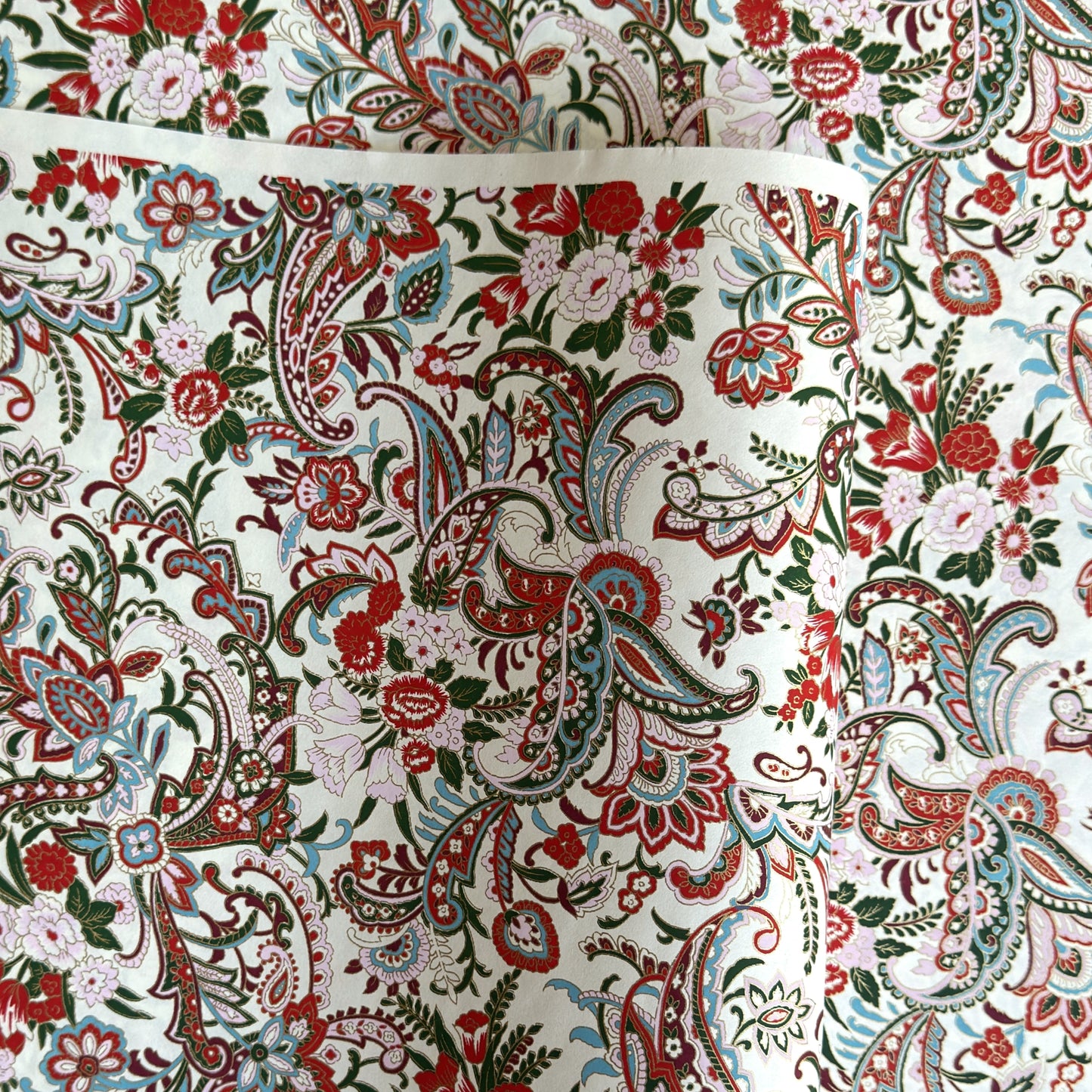 Japanese chiyogami paper silkscreened with a paisley floral style pattern in red, aqua, green and gold on a white background.