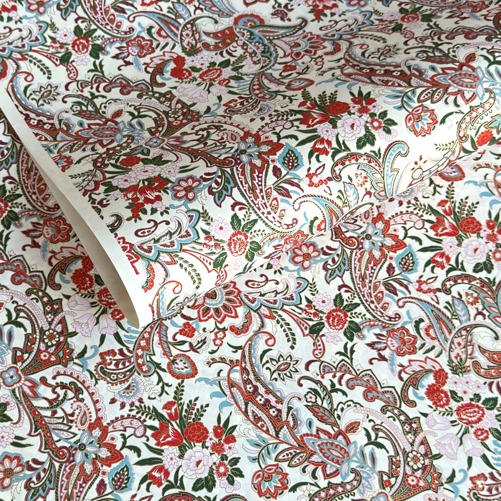 Japanese chiyogami paper silkscreened with a paisley floral style pattern in red, aqua, green and gold on a white background.