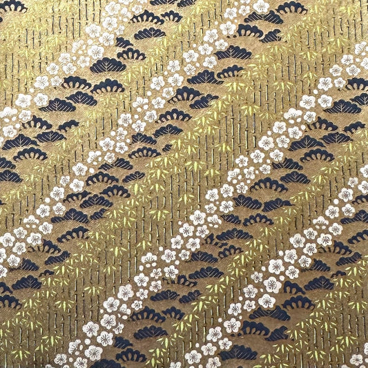 Japanese chiyogami paper with a design of trees, bamboo and plum blossom in indigo, green and white on a vintage gold backdrop. 