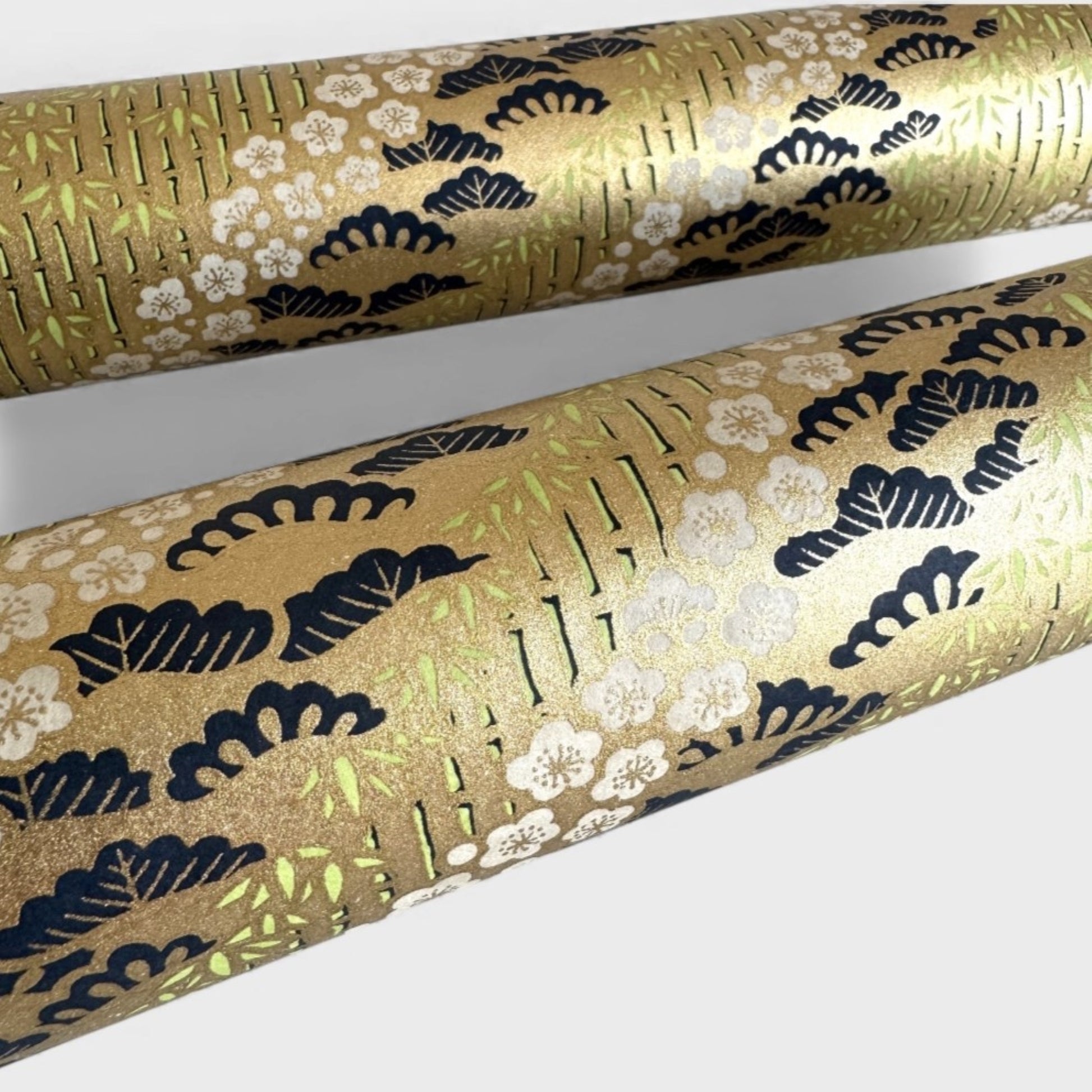 Japanese chiyogami paper with a design of trees, bamboo and plum blossom in indigo, green and white on a vintage gold backdrop.  Close up