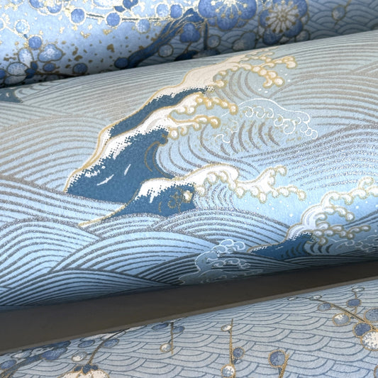 Japanese chiyogami paper with a wave pattern in pale blue, gold and silver. Close-up of a wave