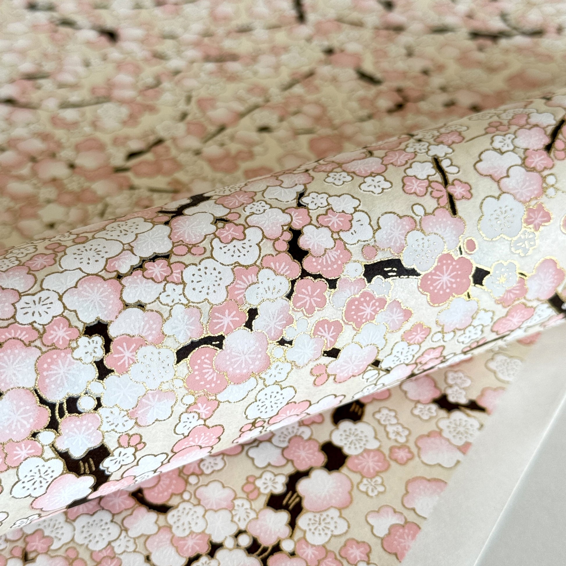 Japanese chiyogami paper with pale pink plum blossom, dark brown branches on an ivory background. Close-up