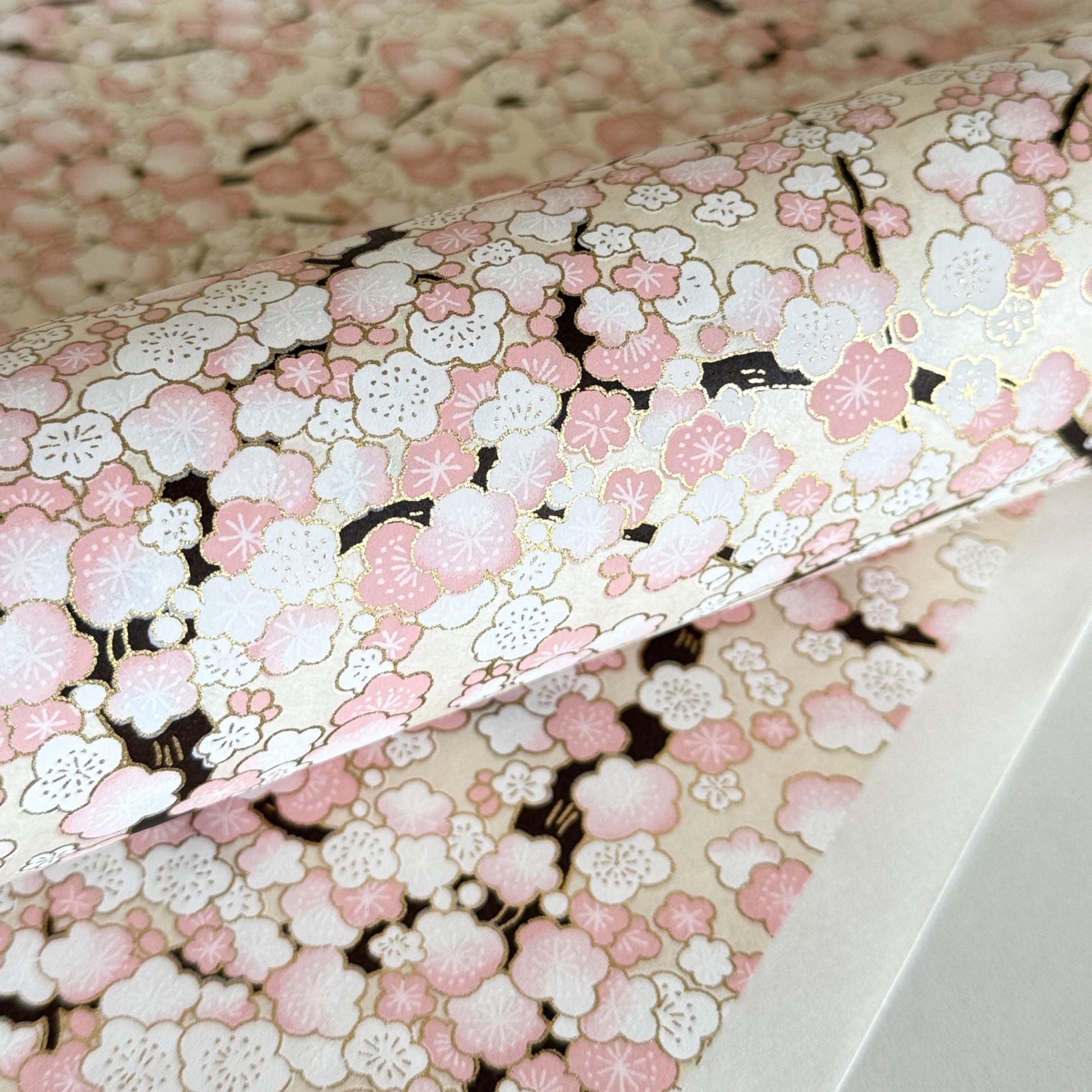 Japanese chiyogami paper with pale pink plum blossom, dark brown branches on an ivory background. Closeup