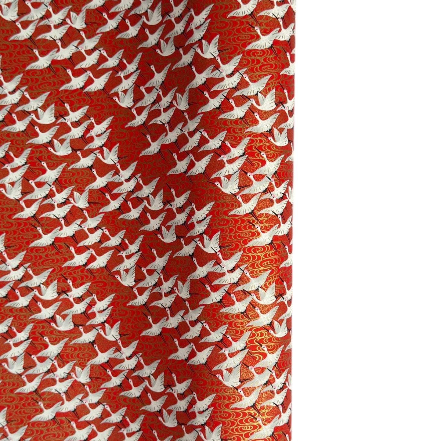 A close-up of a red sheet of Japanese chiyogami paper with an all-over repeating pattern of white cranes and small gold wave-like motifs. 
