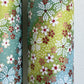 Japanese chiyogami paper silkscreened with a dainty pattern of white sakura flowers on an backdrop of aqua and lime diagonal wavy stripes. Close up