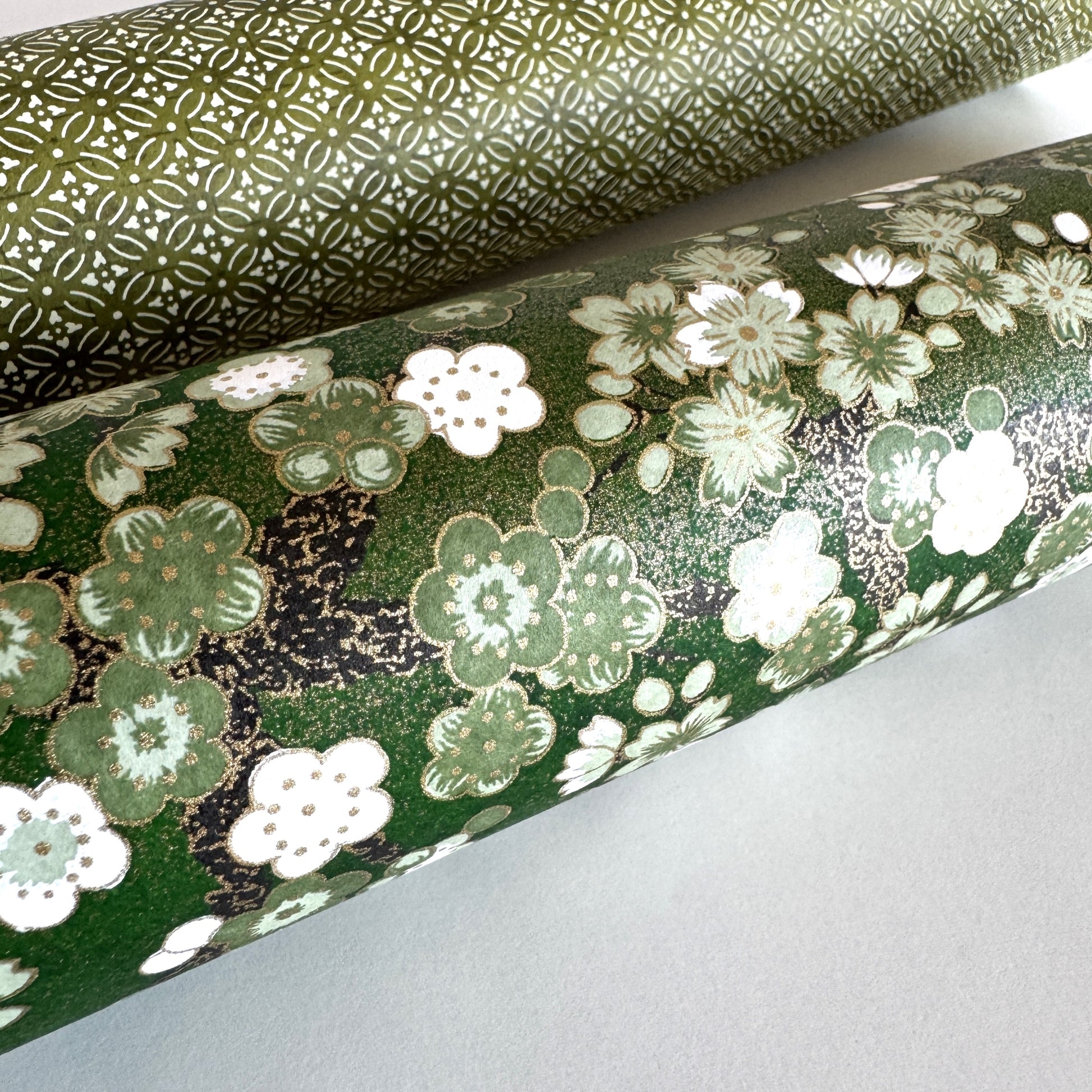 Japanese chiyogami paper with white and pale green blossom flowers on dark green backdrop.