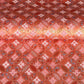 A close-up of a sheet of Japanese chiyogami paper featuring a repeating geometric medallion design in shades of terracotta red, coral pink, and metallic gold