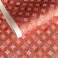 A close-up of a sheet of Japanese chiyogami paper featuring a repeating geometric medallion design in shades of terracotta red, coral pink, and metallic gold