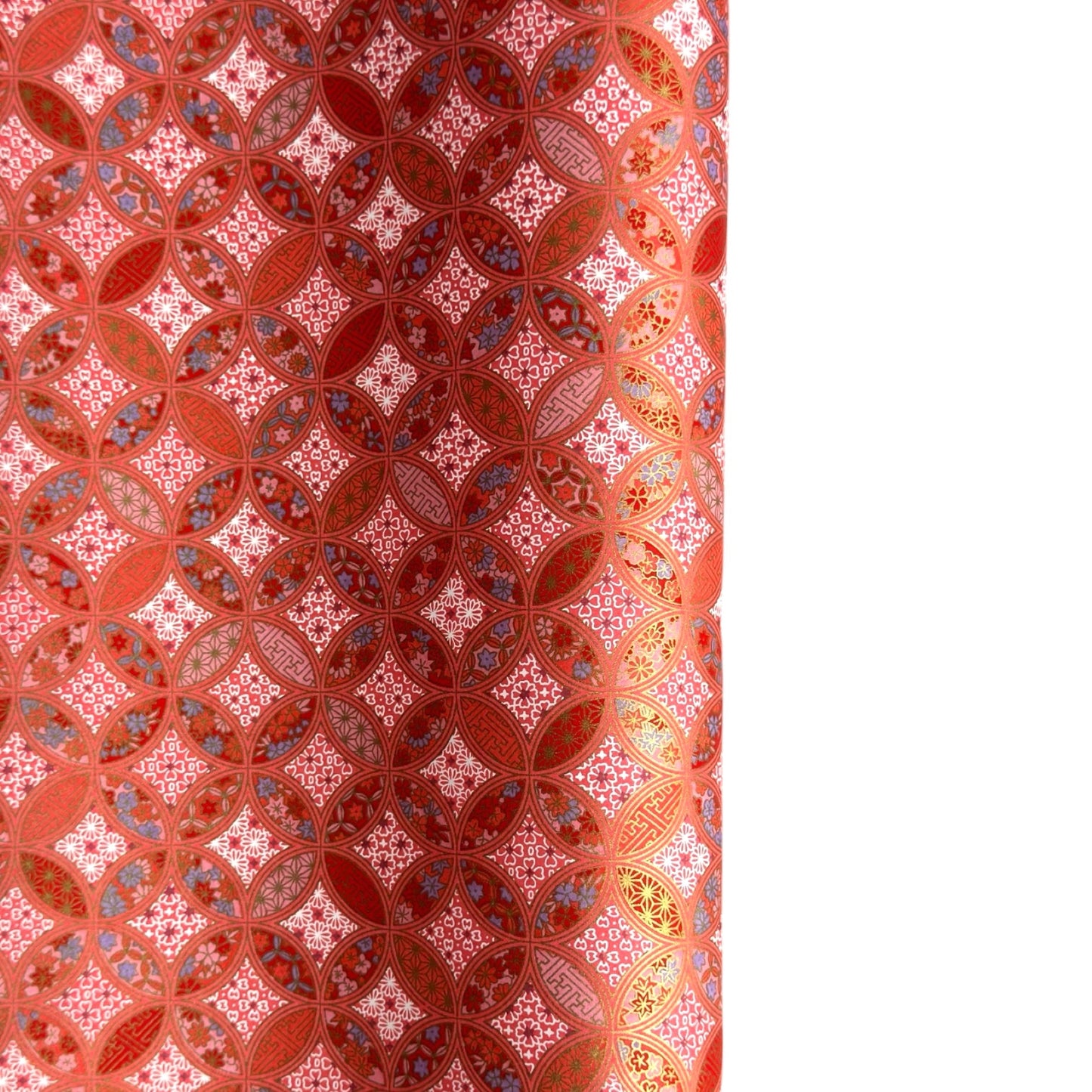 A close-up of a sheet of Japanese chiyogami paper featuring a repeating geometric medallion design in shades of terracotta red, coral pink, and metallic gold