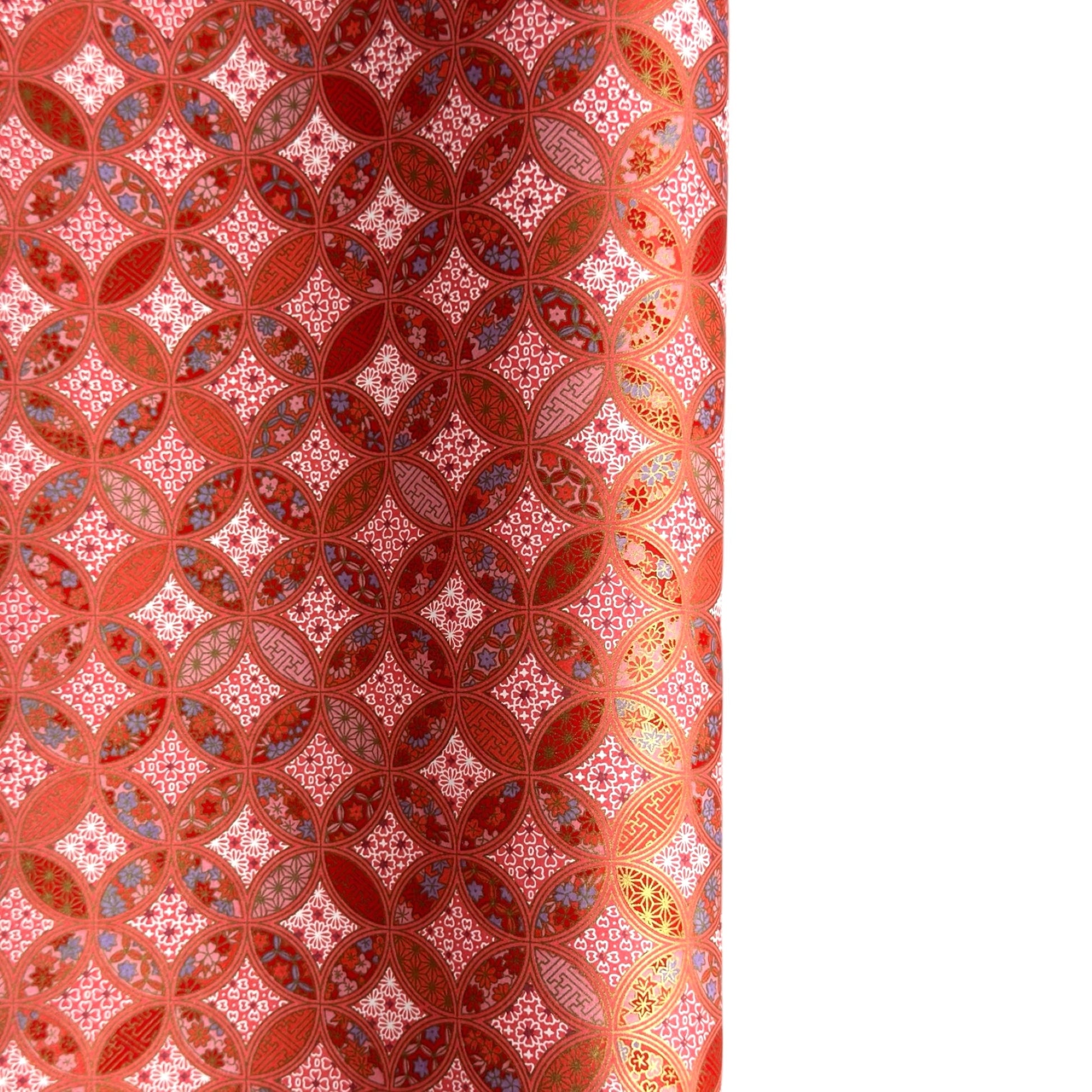 A close-up of a sheet of Japanese chiyogami paper featuring a repeating geometric medallion design in shades of terracotta red, coral pink, and metallic gold