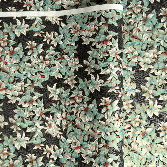 a sheet of Japanese chiyogami screen printed paper with a pattern of light green foliage on a black ground with silver botanical details
