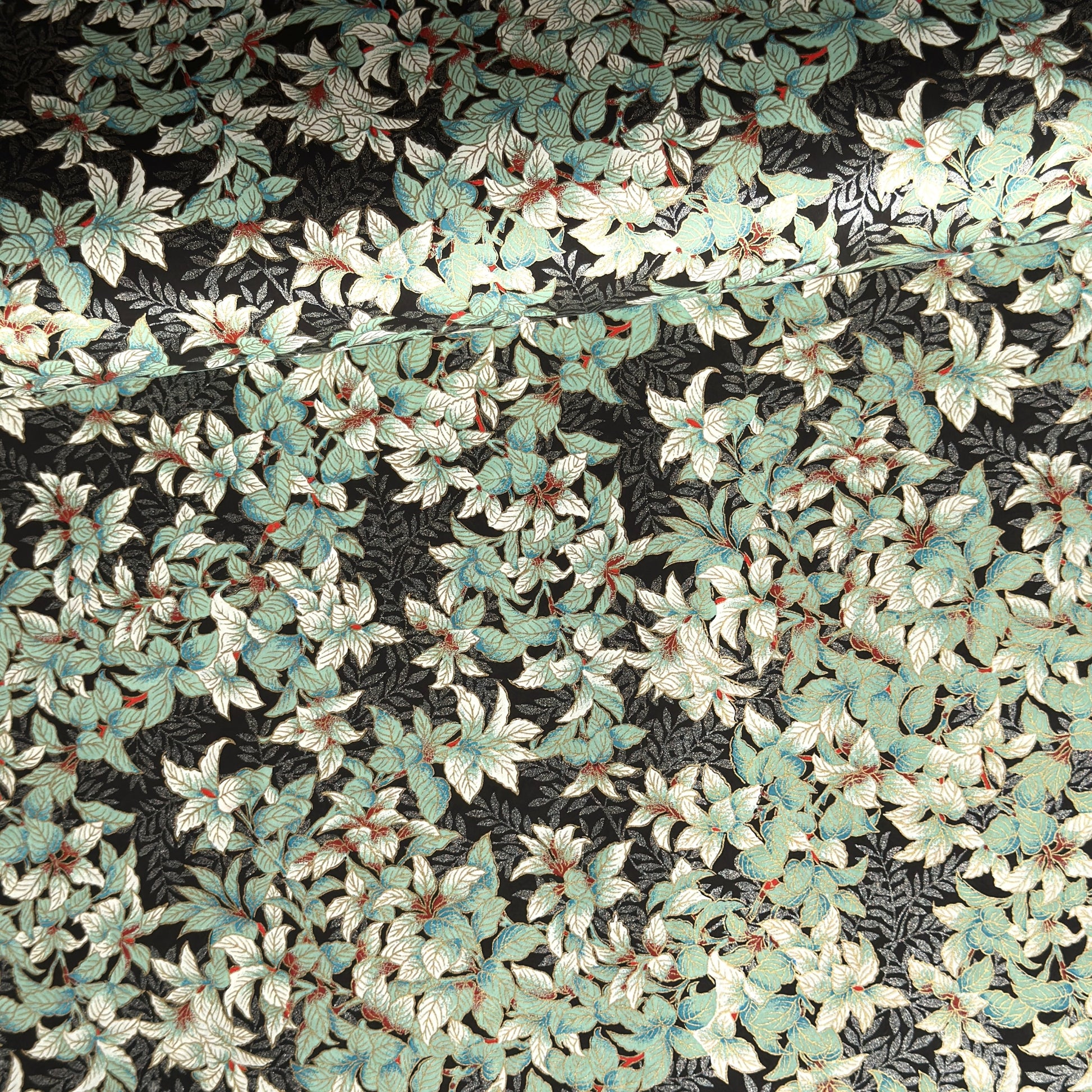 a sheet of Japanese chiyogami screen printed paper with a pattern of light green foliage on a black ground with silver botanical details