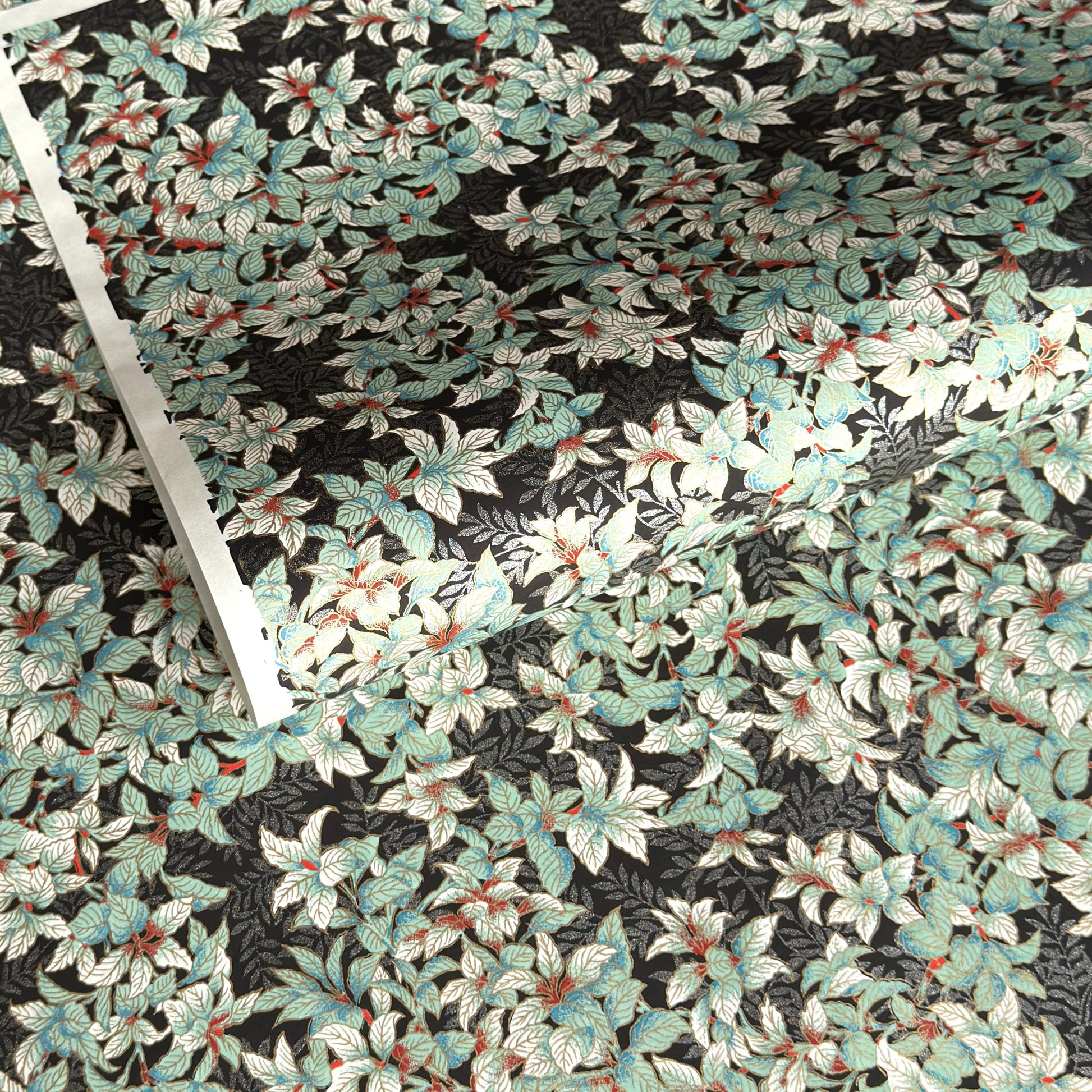 a sheet of Japanese chiyogami screen printed paper with a pattern of light green foliage on a black ground with silver botanical details