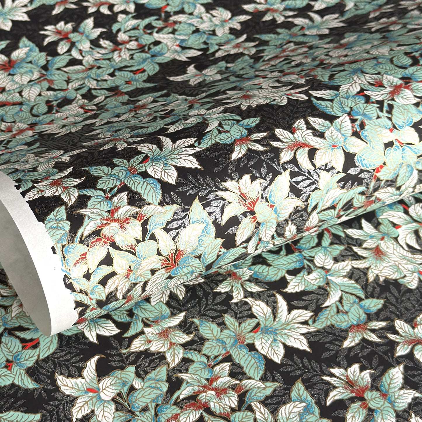 a sheet of Japanese chiyogami screen printed paper with a pattern of light green foliage on a black ground with silver botanical details