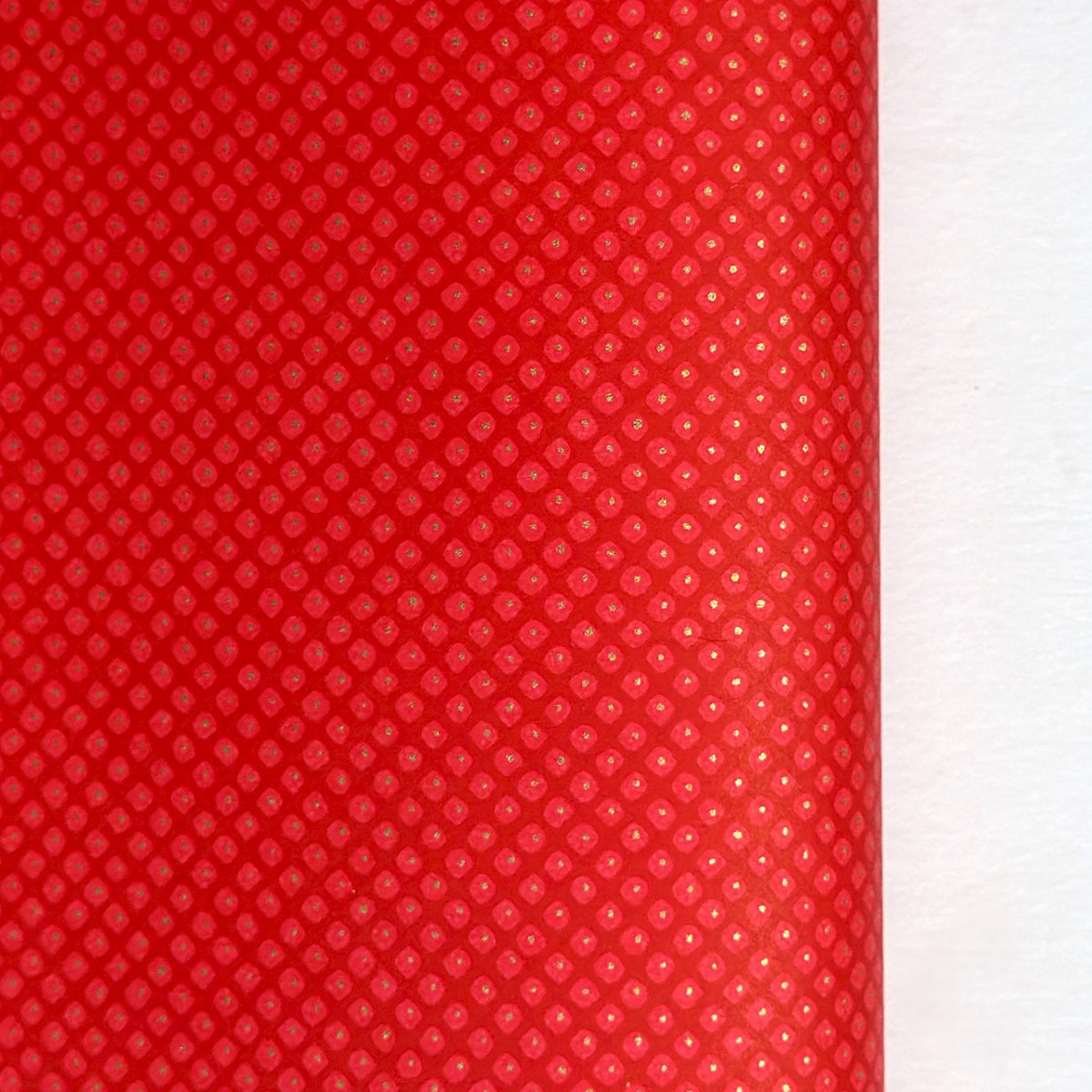 A close-up of a bright red sheet of chiyogami paper with a fine dotted pattern in gold. 