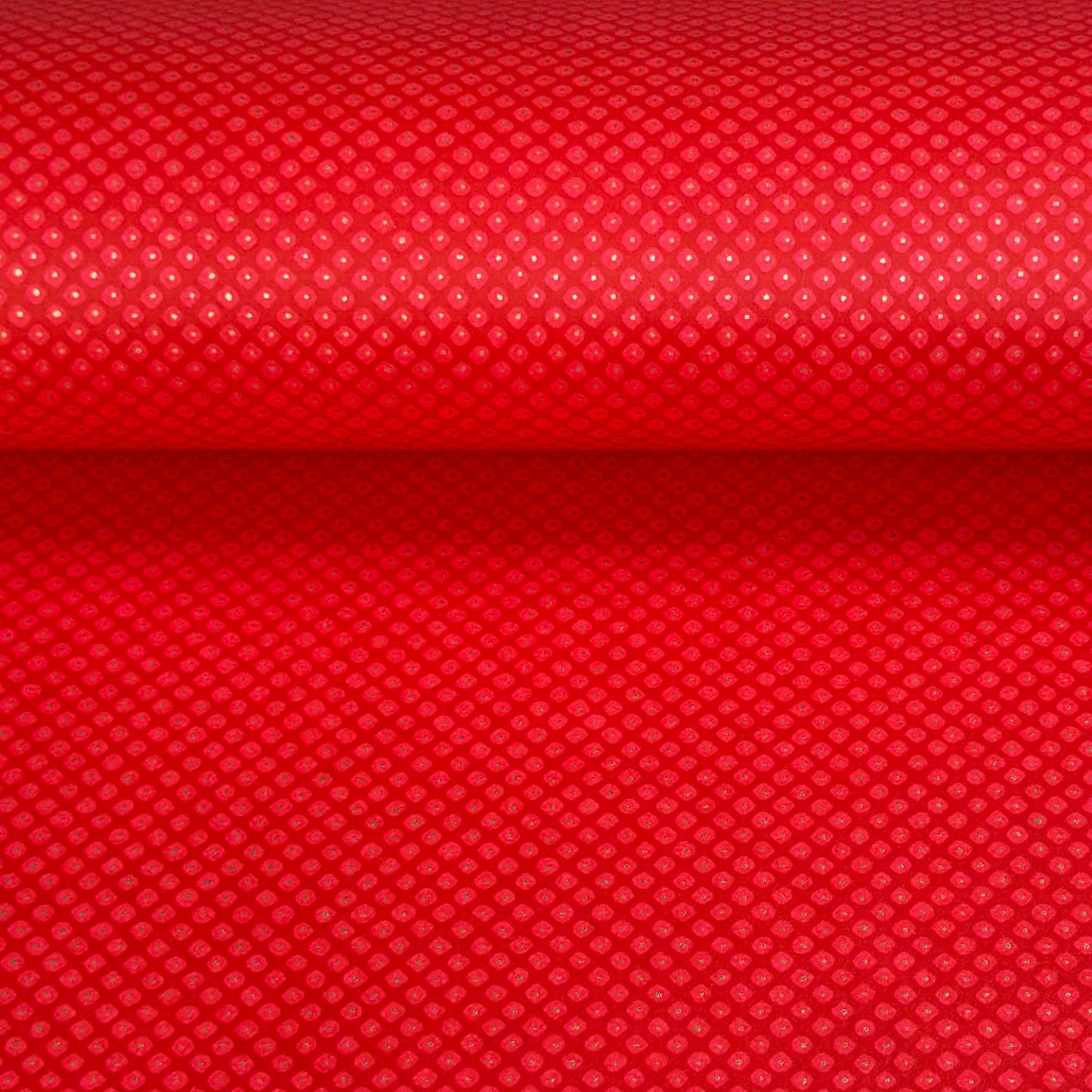 A close-up of a bright red sheet of chiyogami paper with a fine dotted pattern in gold. 