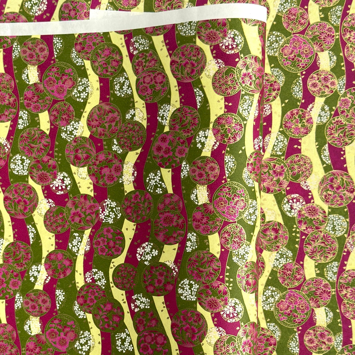 a sheet of Japanese chiyogami yuzen paper with wavy stripes in magenta, green and yellow, overlaid with circles with delicate flowers in the middle and outlined in gold.