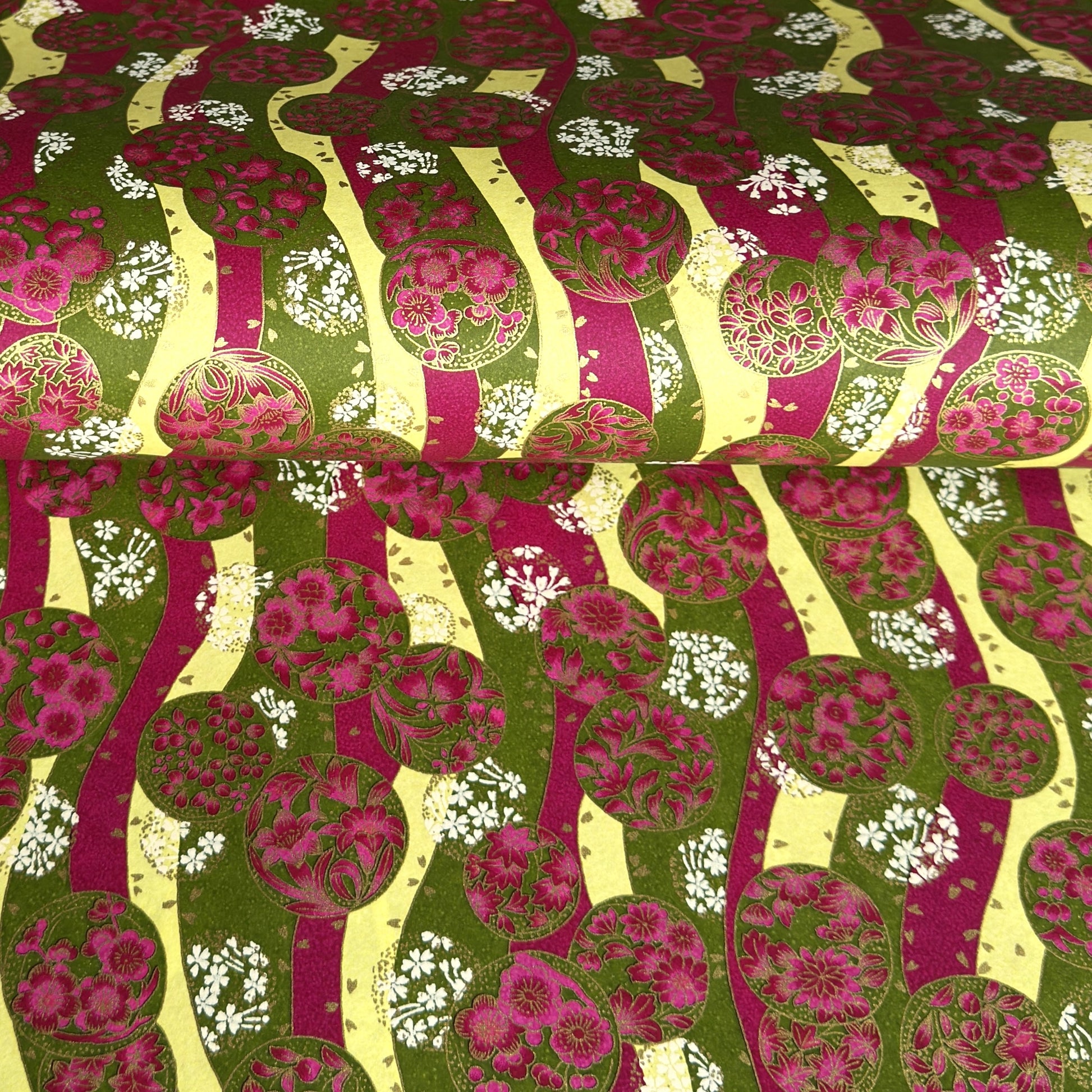 a sheet of Japanese chiyogami yuzen paper with wavy stripes in magenta, green and yellow, overlaid with circles with delicate flowers in the middle and outlined in gold.