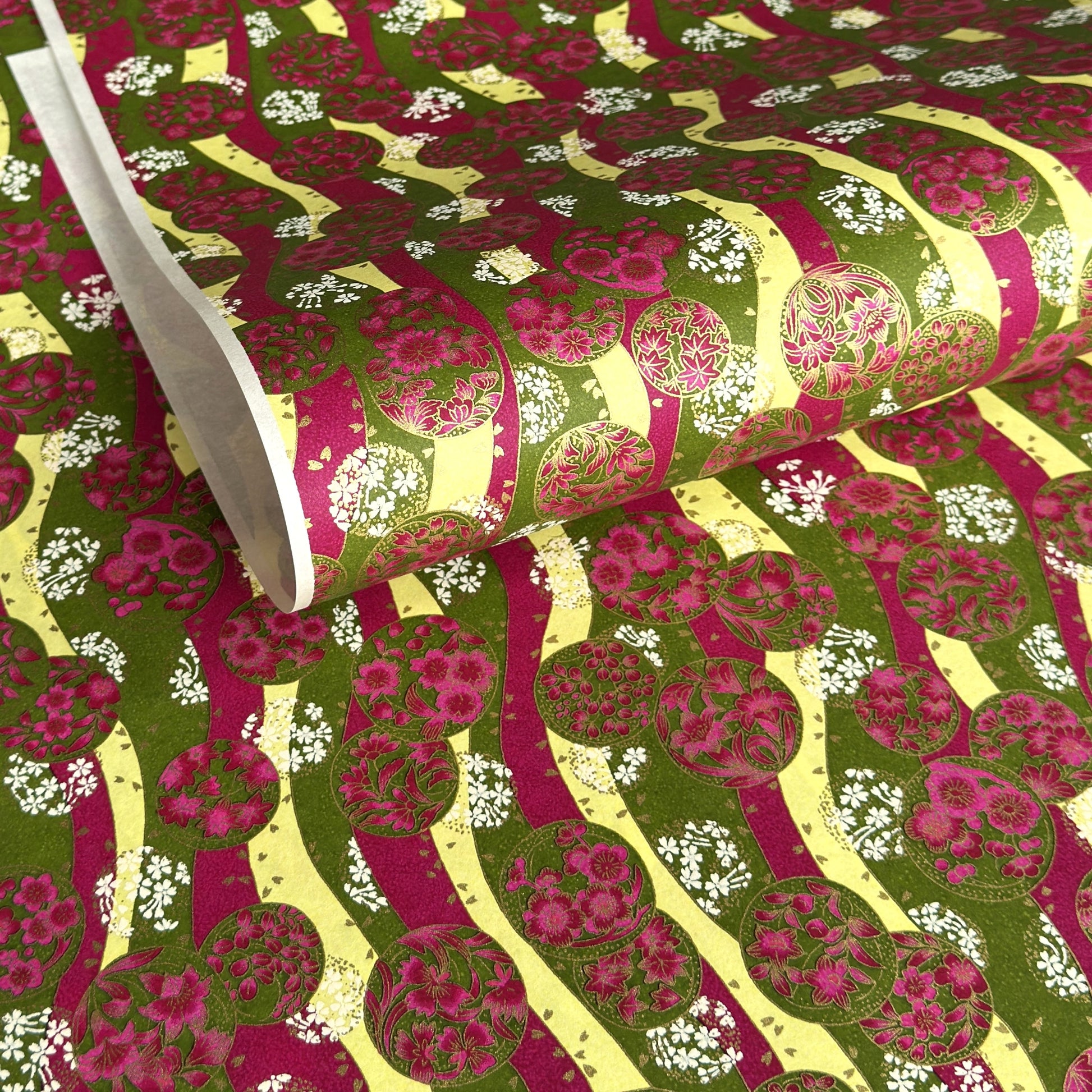 a sheet of Japanese chiyogami yuzen paper with wavy stripes in magenta, green and yellow, overlaid with circles with delicate flowers in the middle and outlined in gold.