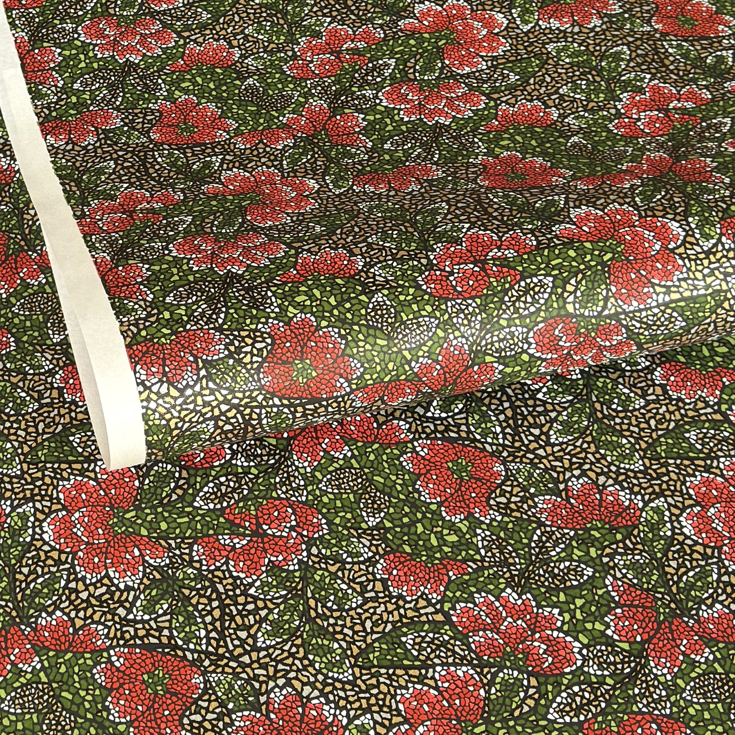 A close-up of a sheet of Japanese chiyogami paper with a repeating mosaic floral print. The design features red and flowers, green leaves on a black and gold mosaic background.