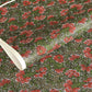 A close-up of a sheet of Japanese chiyogami paper with a repeating mosaic floral print. The design features red and flowers, green leaves on a black and gold mosaic background.