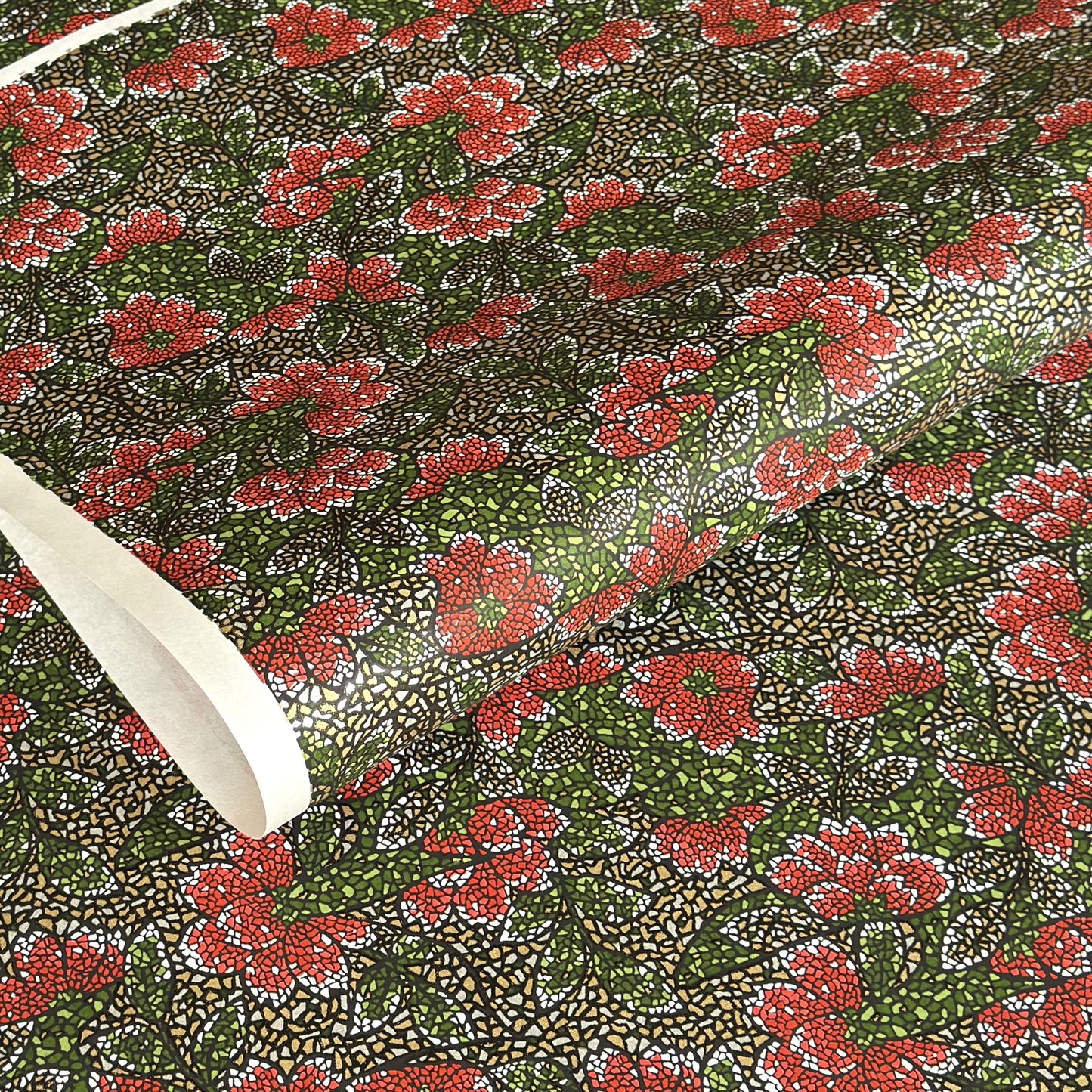 A close-up of a sheet of Japanese chiyogami paper with a repeating mosaic floral print. The design features red and flowers, green leaves on a black and gold mosaic background.