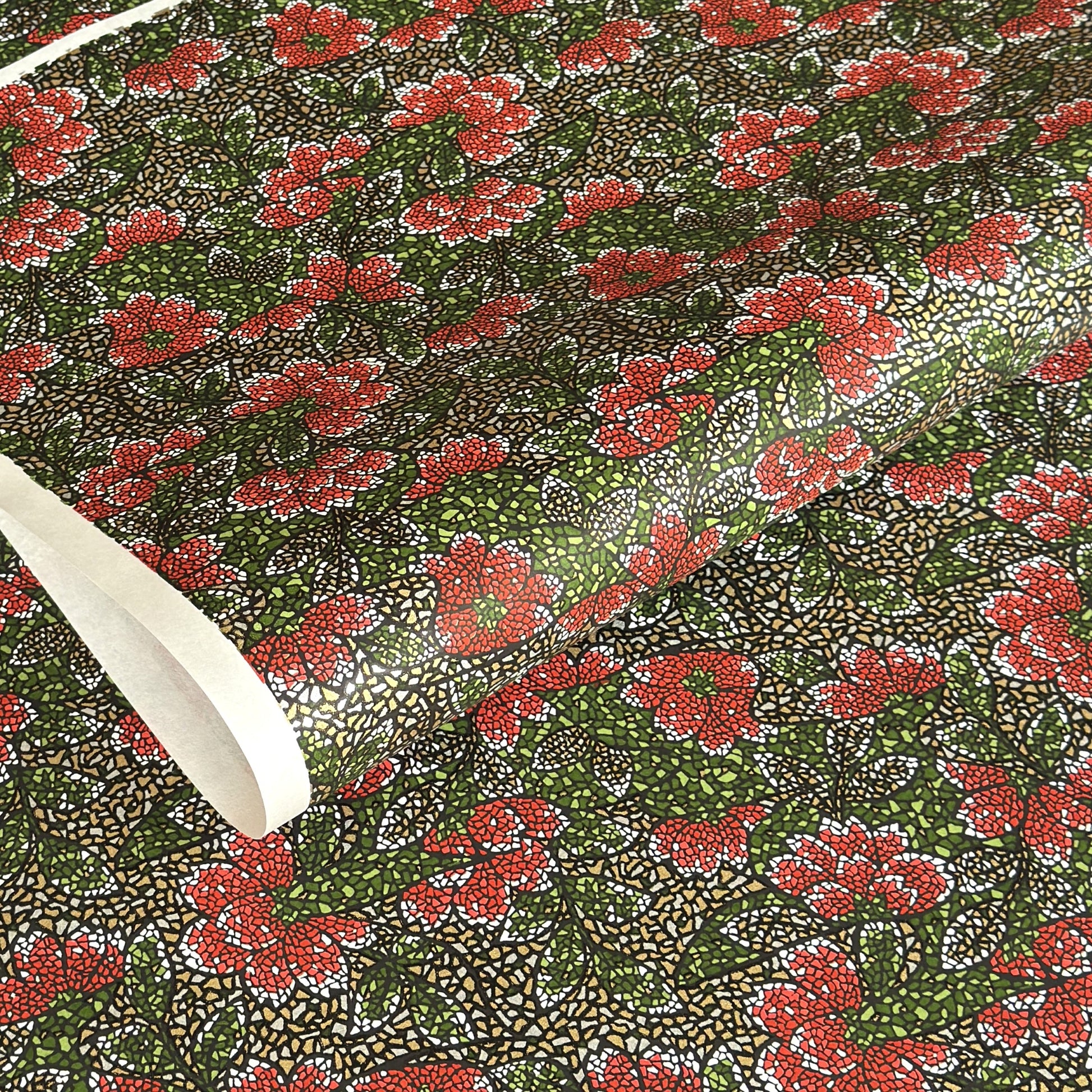 A close-up of a sheet of Japanese chiyogami paper with a repeating mosaic floral print. The design features red and flowers, green leaves on a black and gold mosaic background.
