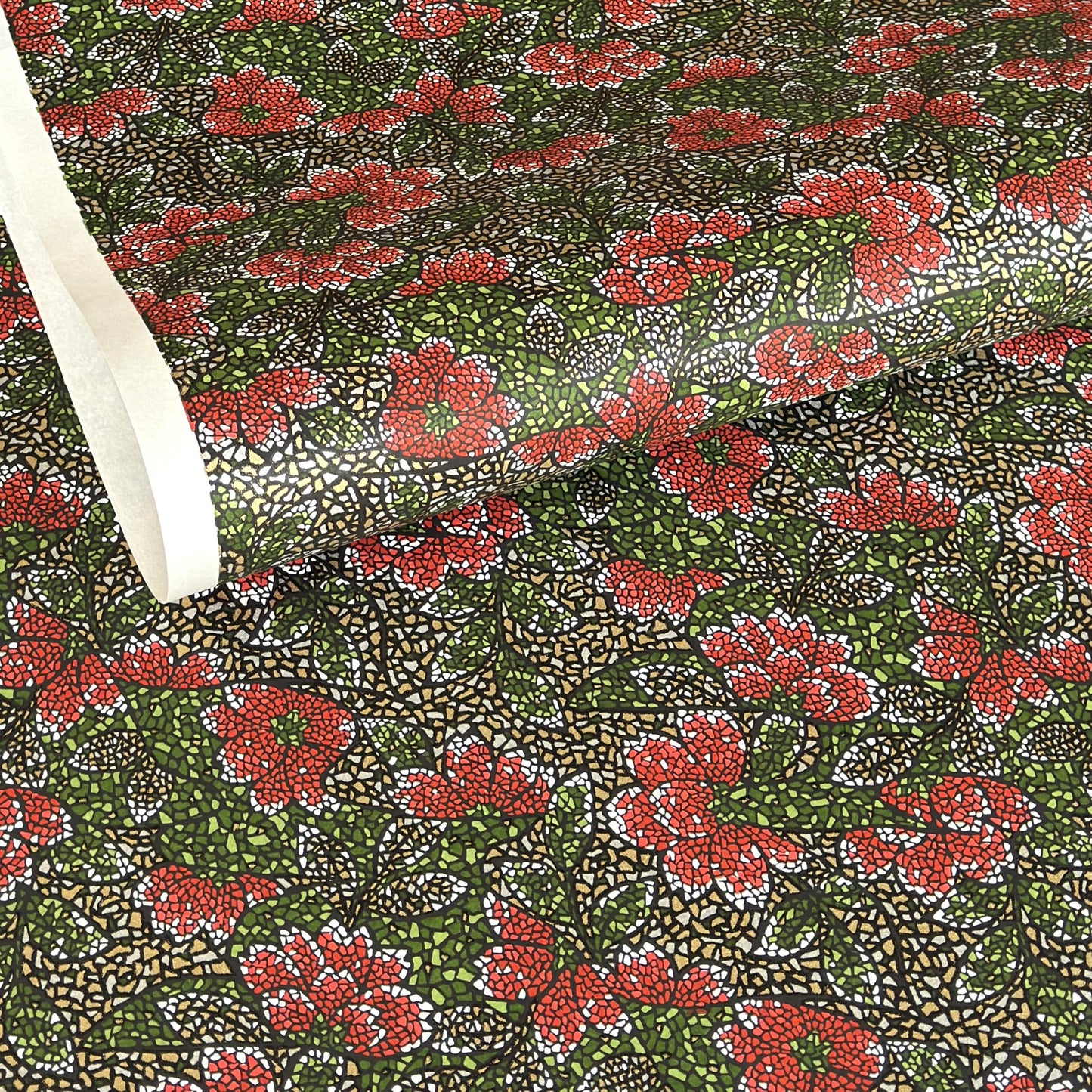 A close-up of a sheet of Japanese chiyogami paper with a repeating mosaic floral print. The design features red and flowers, green leaves on a black and gold mosaic background.
