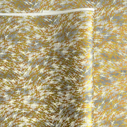 a sheet of Japanese yuzen chiyogami paper with a pattern of a flock of lots of birds flying. Birds are white, gold or copper in colour and flying on a ground of light grey and white sky