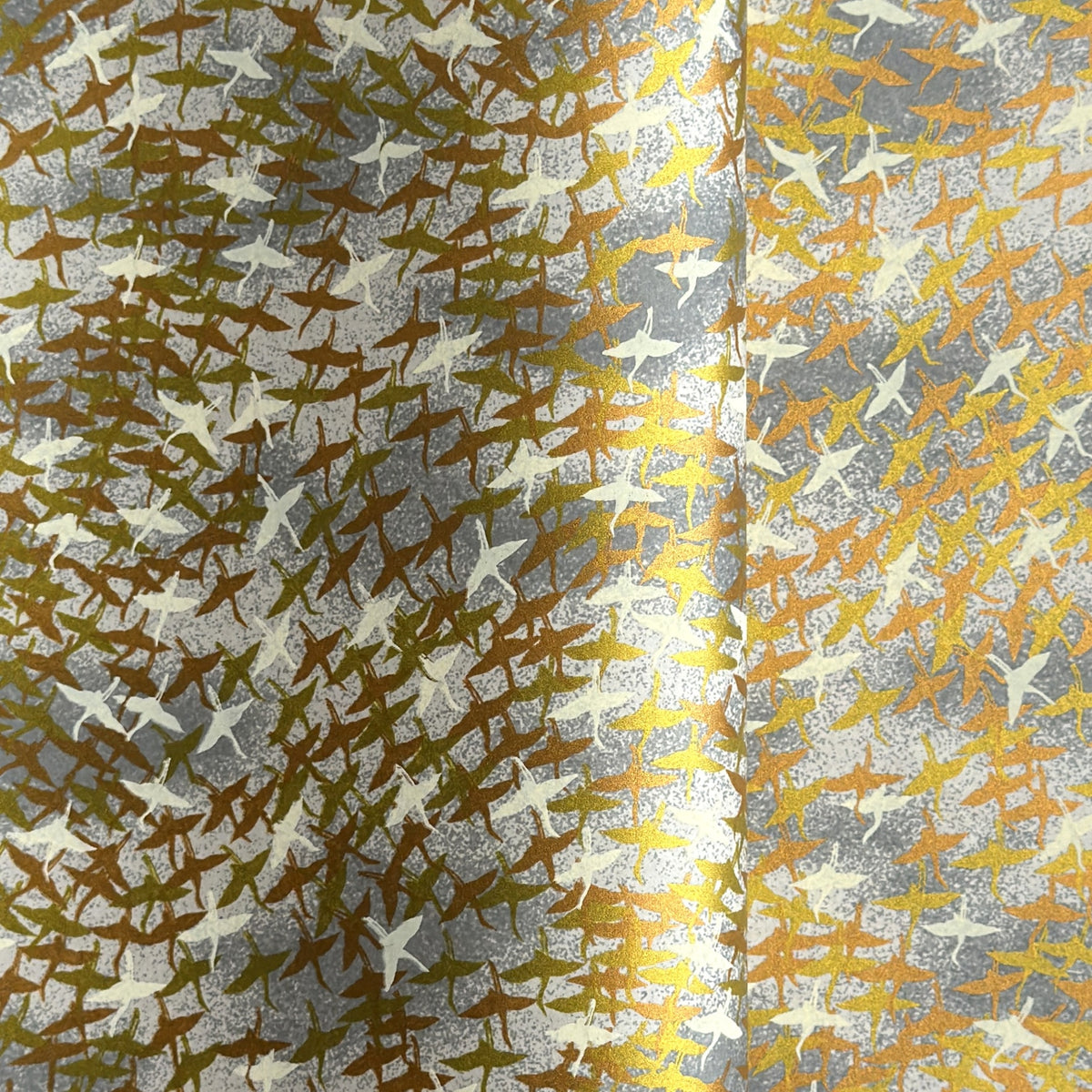 a sheet of Japanese yuzen chiyogami paper with a pattern of a flock of lots of birds flying. Birds are white, gold or copper in colour and flying on a ground of light grey and white sky