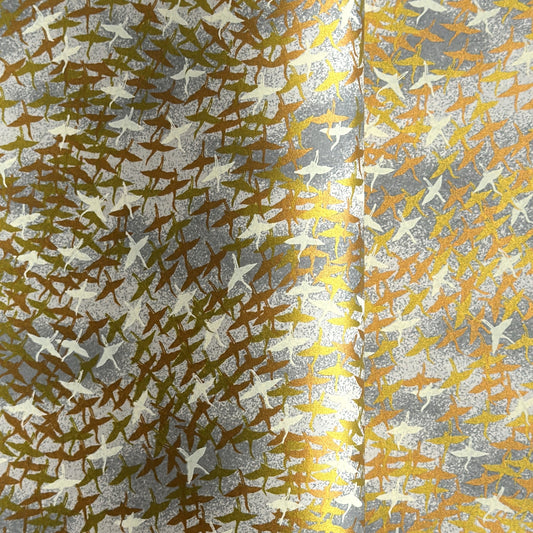 a sheet of Japanese yuzen chiyogami paper with a pattern of a flock of lots of birds flying. Birds are white, gold or copper in colour and flying on a ground of light grey and white sky