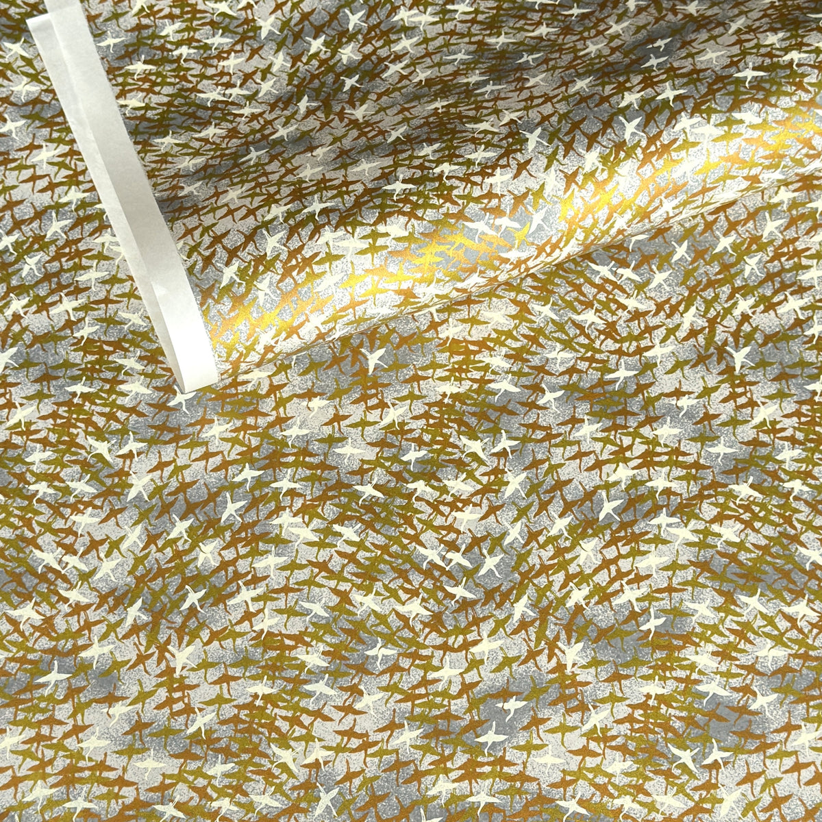a sheet of Japanese yuzen chiyogami paper with a pattern of a flock of lots of birds flying. Birds are white, gold or copper in colour and flying on a ground of light grey and white sky