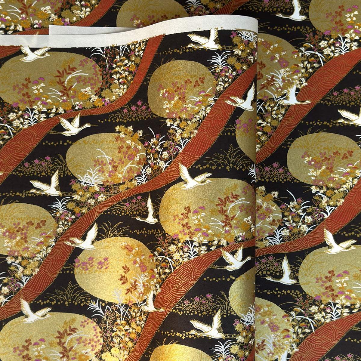 a sheet of Japanese yuzen chiyogami paper in white cranes, flowers and rivers in muted tones of autumn colours and lots of gold on a black ground.